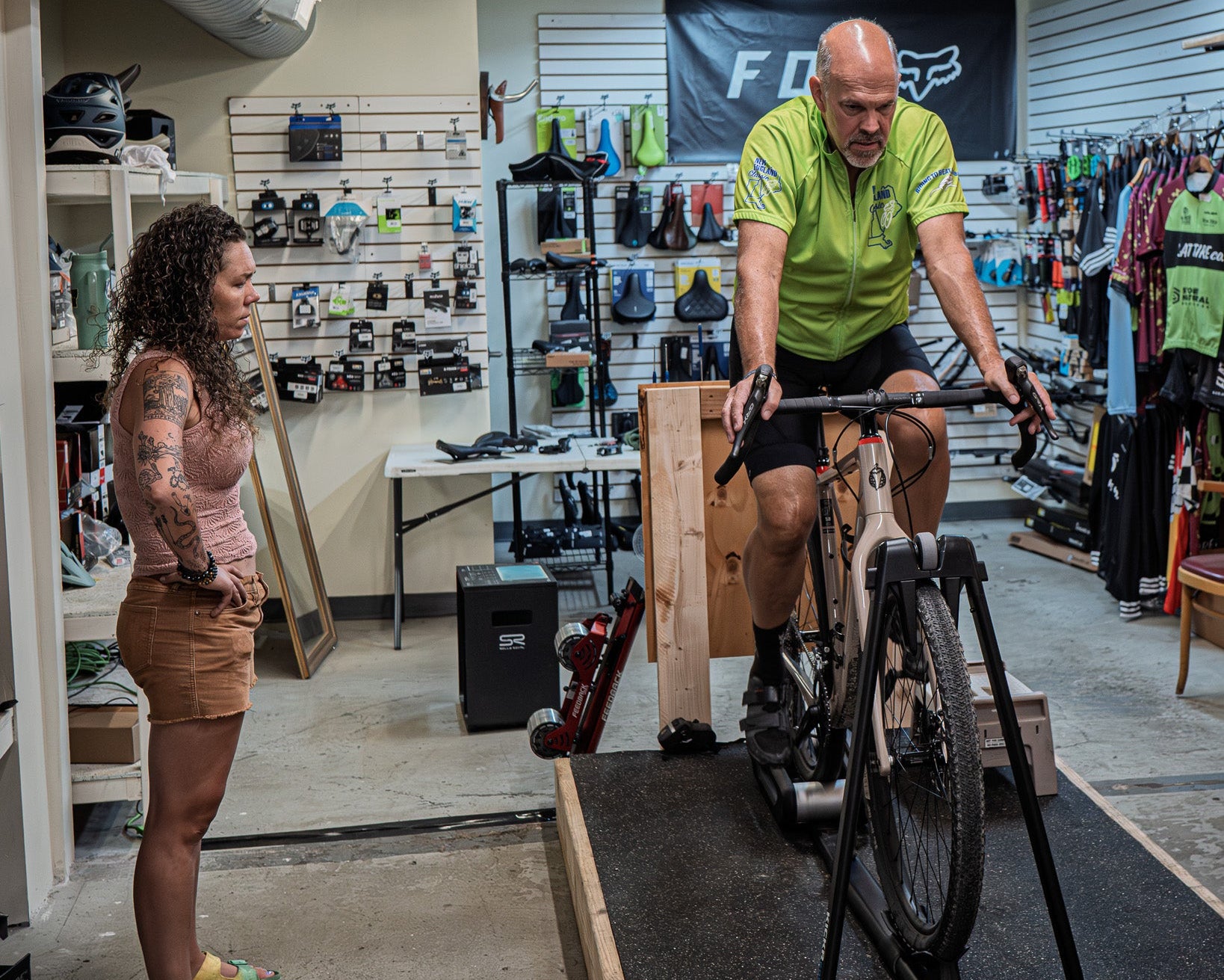 Man using a stationary bike indoors with a woman observing, in a store setting. Bike Fit Greensburg, PA