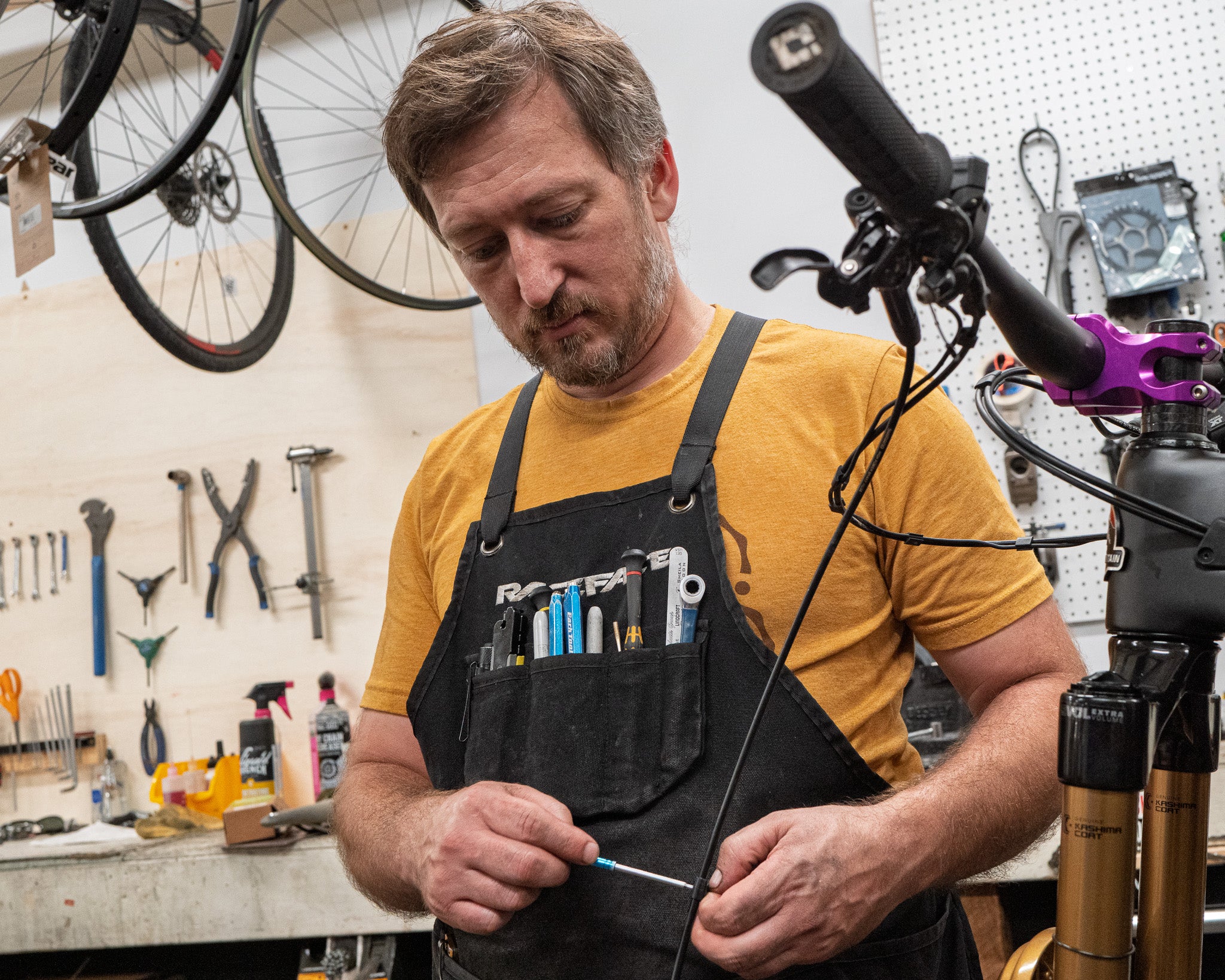 Man working on a bicycle in a workshop with tools and equipment around.